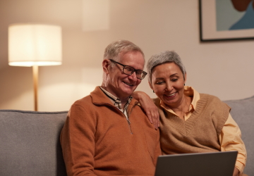 An older couple smiling which looking at something on a laptop