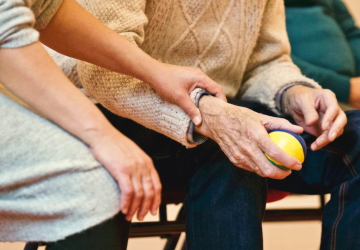 A care home worker holding the hand of a patent steady while they hold a ball