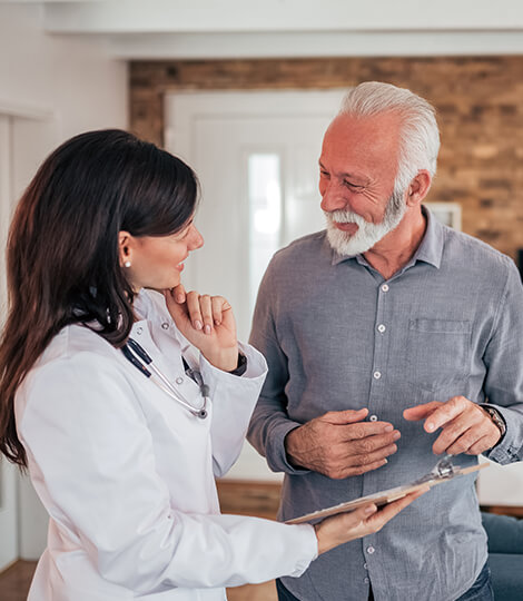 An older gentleman discussing health care requirements with a female doctor holding a clipboard
