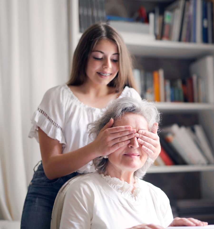 A young woman playfully covering her grandmothers eyes while smiling